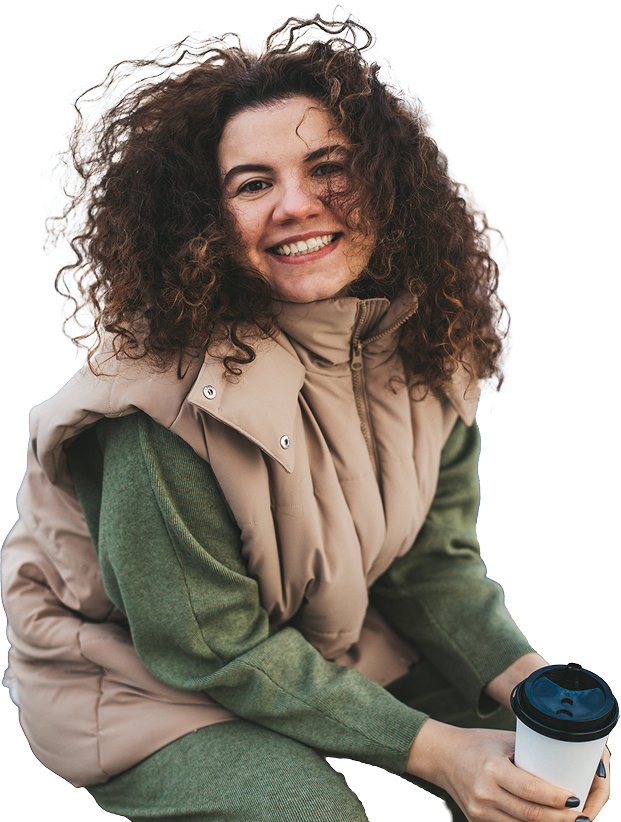 Jeune femme aux cheveux bouclés, heureuse, avec un café en plein air.